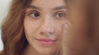 微笑女人应用保湿奶油脸皮肤前面浴室镜子